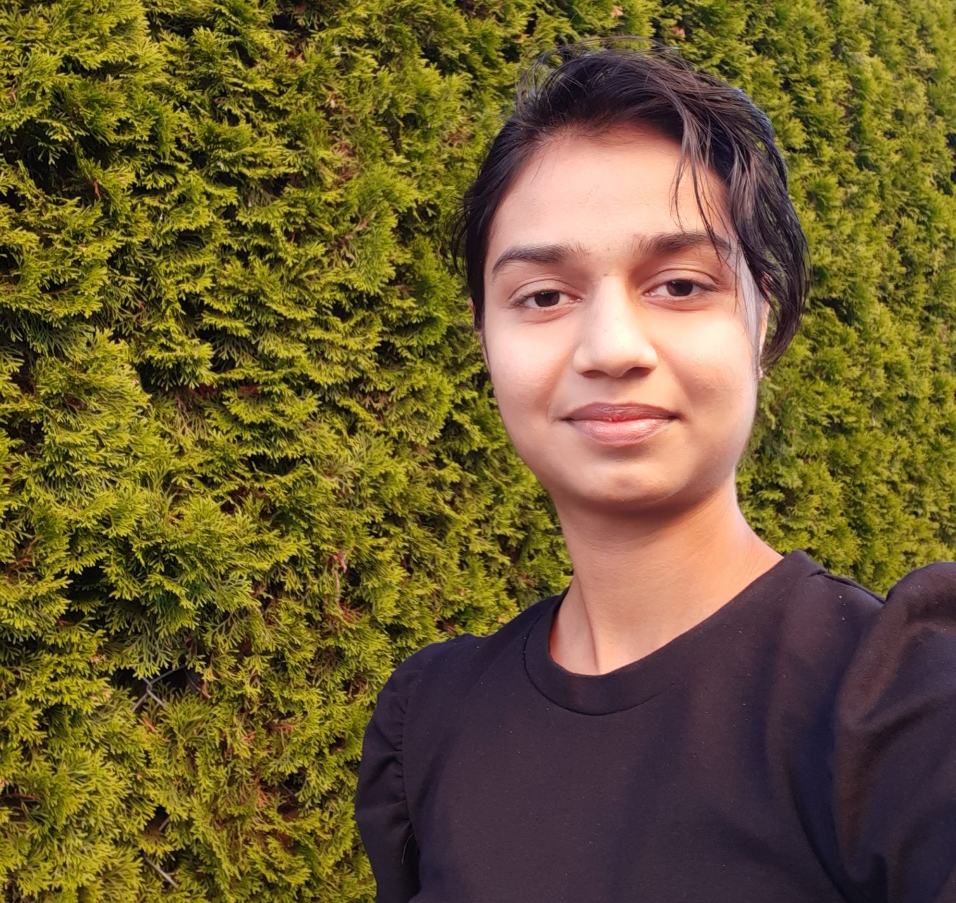 Selfie en plein air de Pallavi G. portant un t-shirt avec du feuillage en arrière-plan.